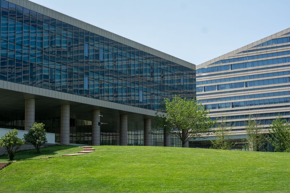 A modern commercial office building in Hurlingham estate Fulham featuring a sleek facade composed of large glass panels and white concrete vertical fins. The building's exterior shows reflective blue-